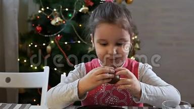 圣诞前夜坐在圣诞树旁吃巧克力圣诞老人的女孩。 在家庆祝圣诞节